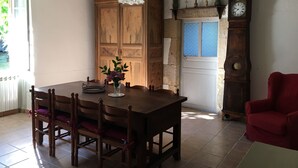Un coin repas avec une table en bois, des chaises, un vase de fleurs, un meuble en bois, une horloge et une chaise rouge.