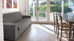 A room with a grey sofa, wooden dining table, chairs, and a sliding glass door leading to a garden. - N082 - Numana, villa with right garden (Numana)