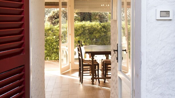 An open door leading to a patio with a table and chairs, a view of greenery, and a white wall with a thermostat. - N082 - Numana, villa with right garden (Numana)