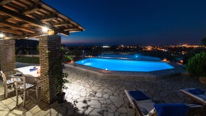 Zona de piscina exterior con suelo de piedra, sillones de descanso y una mesa bajo una pérgola de madera.
