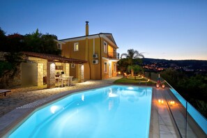 Una casa de dos pisos con piscina, patio de piedra y zona de estar al aire libre.