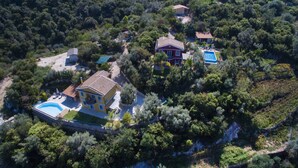 Vista aérea de una propiedad con piscina, una casa grande con balcón y vegetación exuberante a su alrededor.