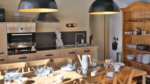 A modern kitchen with wooden cabinets, a built-in oven, and a dining area set for six with a table, chairs, and various kitchenware.