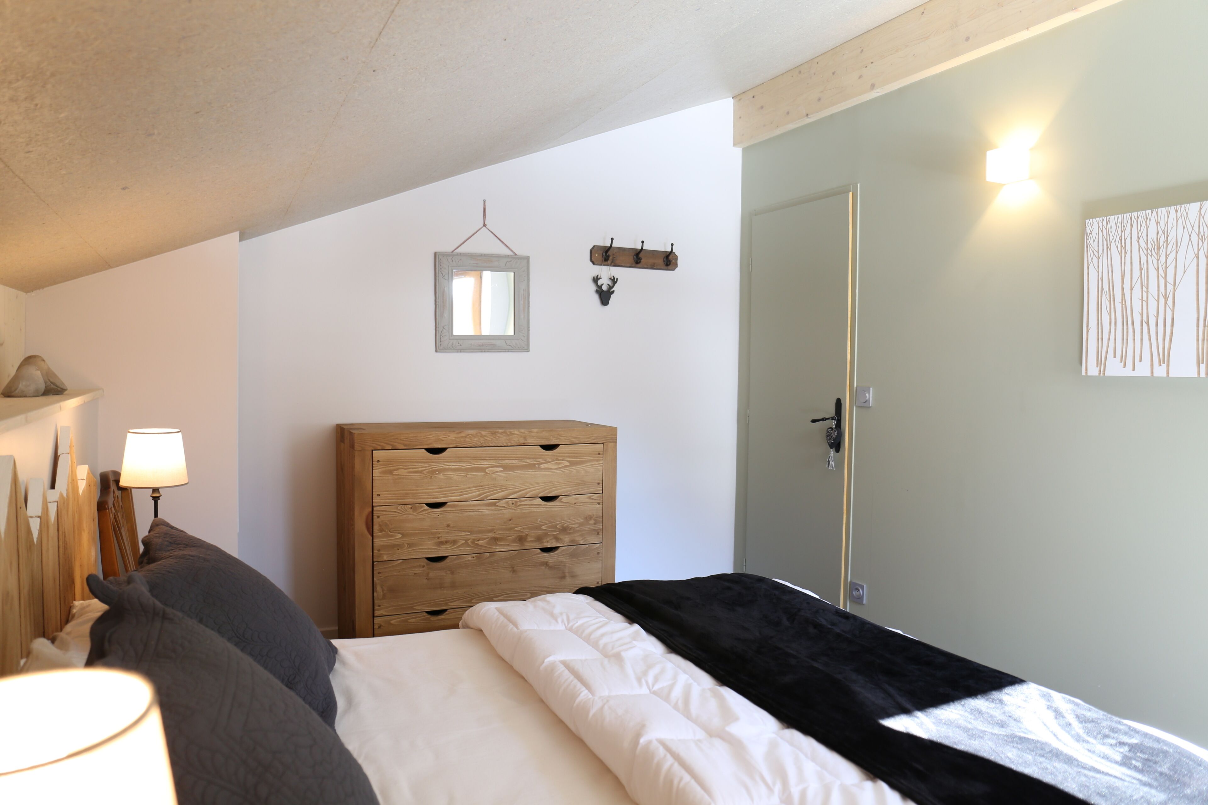 A bedroom with a bed, wooden dresser, wall-mounted light, and a door.