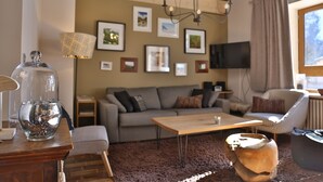 A living room with a sofa, a coffee table, a lamp, a TV, and framed pictures on the wall.
