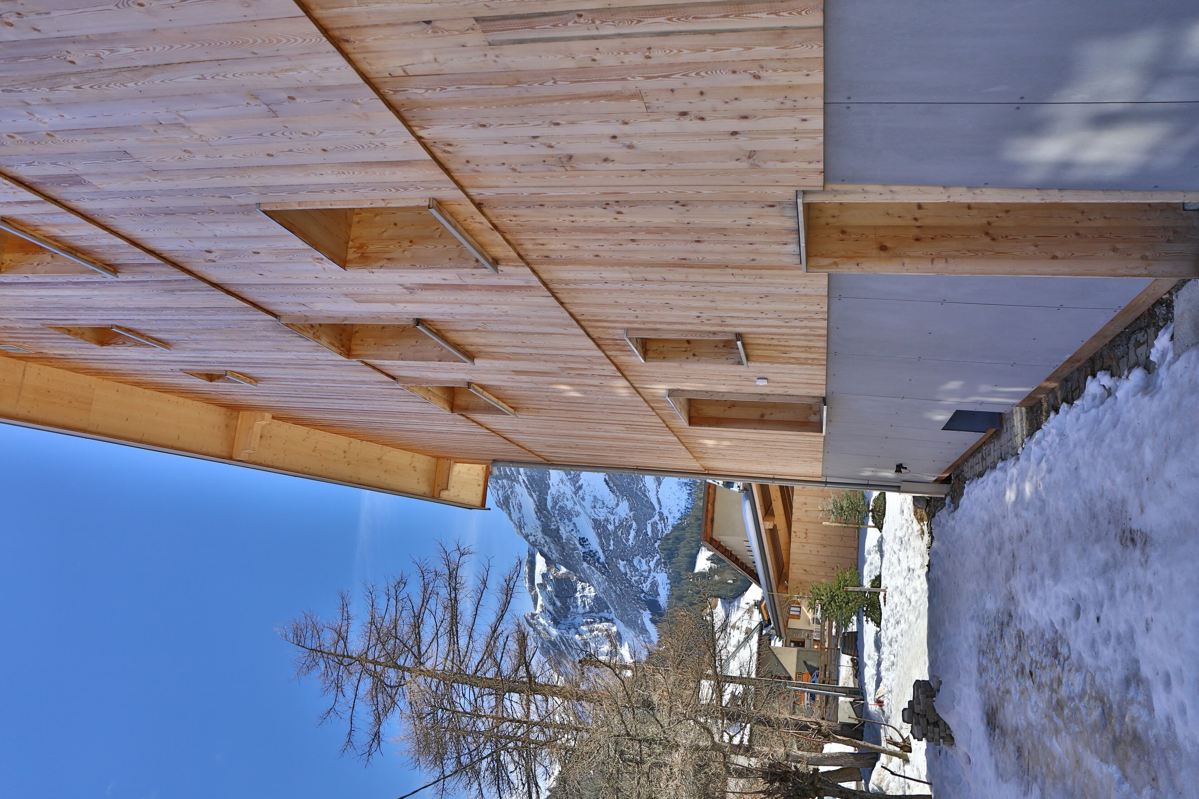 Une structure de plafond en bois avec des poutres apparentes et un sol recouvert de neige.