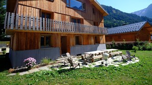 A wooden chalet with a balcony, outdoor seating, and a view of mountains.