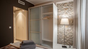 A bedroom with a bed, a wardrobe, a lamp, and a stone wall.