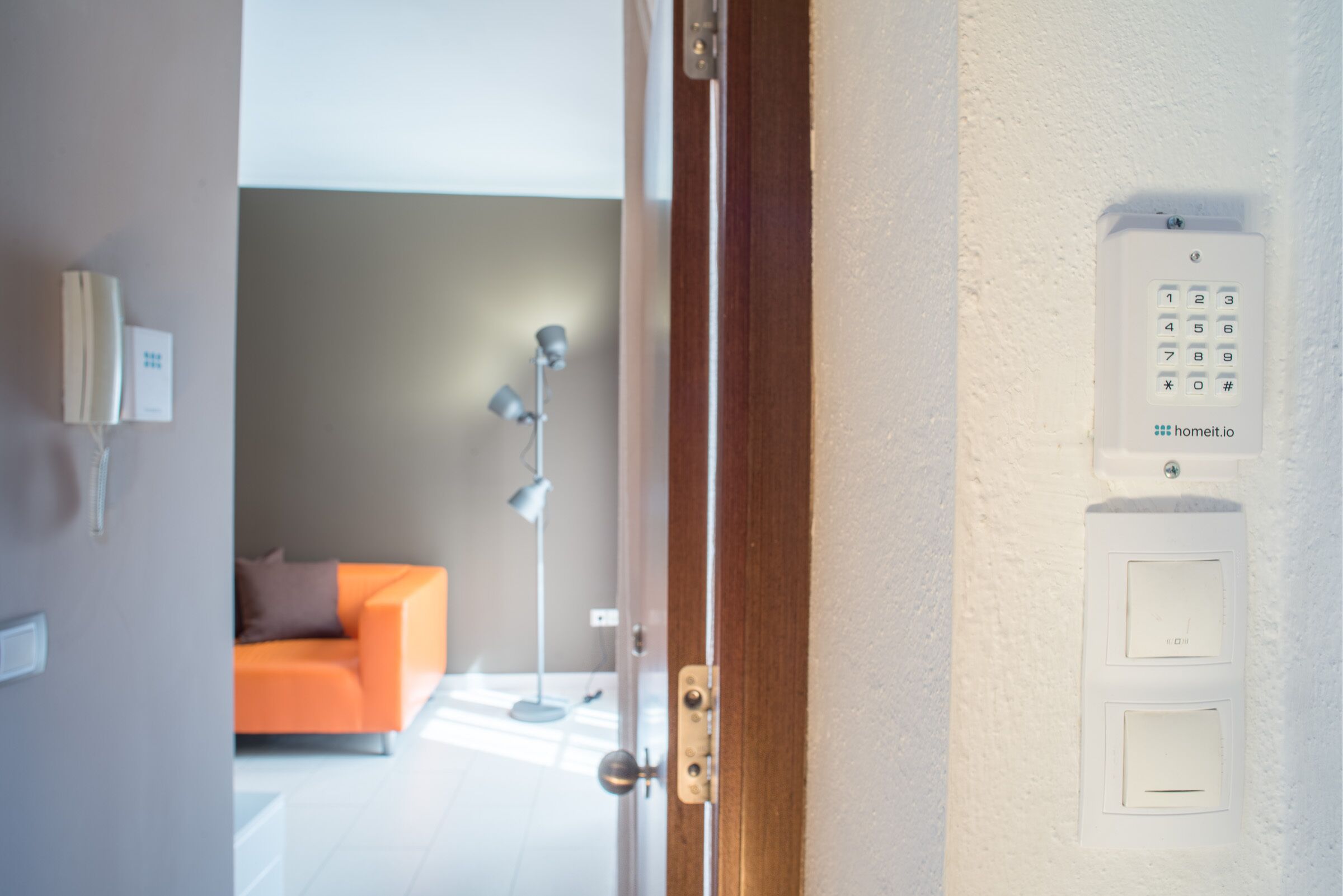 Une vue intérieure d’une chambre d’hôtel, avec une porte en bois, un téléphone blanc fixé au mur et un clavier numérique.