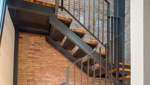 A staircase with wooden steps and metal railings leading to a loft area with a wooden table.