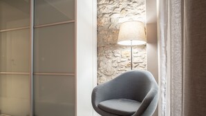 A modern room with a grey chair, a lamp, and a stone wall.