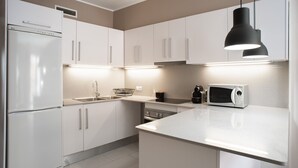 A modern kitchen with white cabinetry, a built-in oven, a microwave, and a black pendant light.