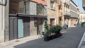 A street view with a row of buildings, including a restaurant named "Ba Restaurant" on the ground floor. There are balconies on the upper floors, and a few potted plants are visible on the sidewalk.