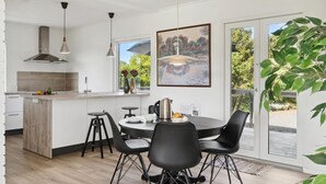 Ett modernt kök med en central köksö, en matplats med stolar och ett stort fönster med en tavla.