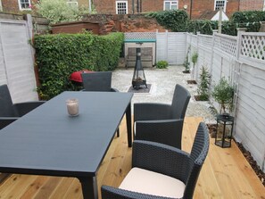 Une terrasse avec une table et des chaises, un barbecue et une clôture blanche.