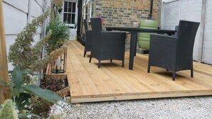 Eine Terrasse mit Holzdeck, schwarzer Rattanmöbel und einer Ziegelwand im Hintergrund.