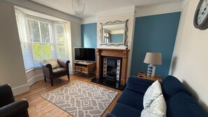 Ein Wohnzimmer mit einem blauen Sofa, einem Fernseher, einem Kamin und einem gemusterten Teppich.