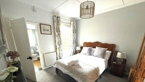 Ein Schlafzimmer mit Bett, Nachttischen, einem Spiegel und einem Fenster mit Vorhängen.