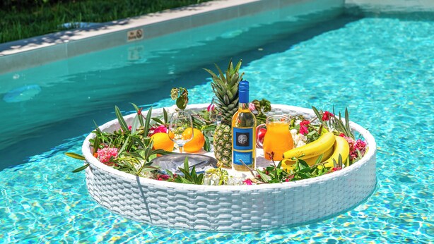 Un décor au bord de la piscine avec un plateau flottant contenant des fruits, des fleurs et des boissons.