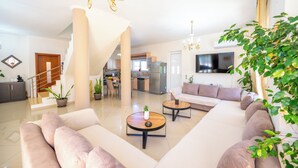 Un vaste espace de vie comprenant un grand canapé, deux tables basses, un escalier, une cuisine et un téléviseur.