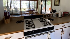 A kitchen with a stove, cabinets, and a dining area with chairs and a table. - Seal Point Waterfront Cottage (Lamoine)