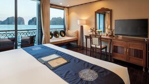 Habitación de hotel con una cama grande, un escritorio con televisor, una silla y vista al mar.