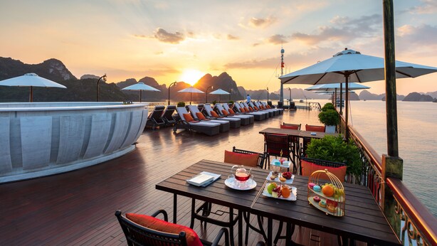 Terraza con sillones de descanso y sombrillas con vista a un cuerpo de agua al atardecer.