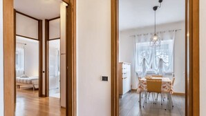 A modern interior with a dining area featuring a table and chairs, a hanging light fixture, and a view through a window with curtains. - The. Loft. by. Guido (Vicenza)