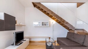 A modern living room with a flat-screen TV, a sofa, a coffee table, and a staircase with glass railings. - The. Loft. by. Guido (Vicenza)