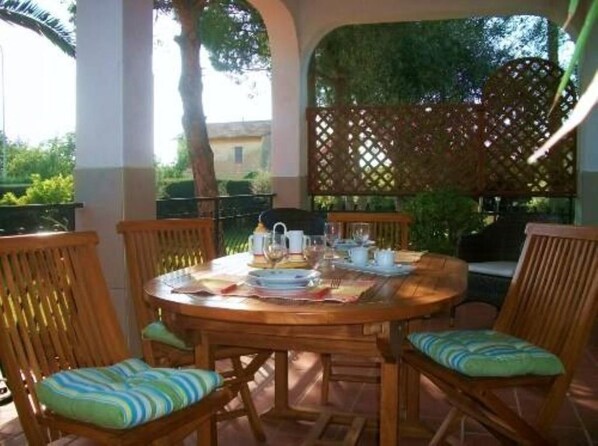 Une table ronde en bois, dressée pour quatre personnes, avec des chaises assorties, un paravent ajouré et une vue sur la verdure.