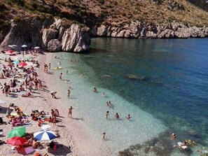 Une plage très fréquentée, avec une eau claire et peu profonde, et des falaises rocheuses en arrière-plan.