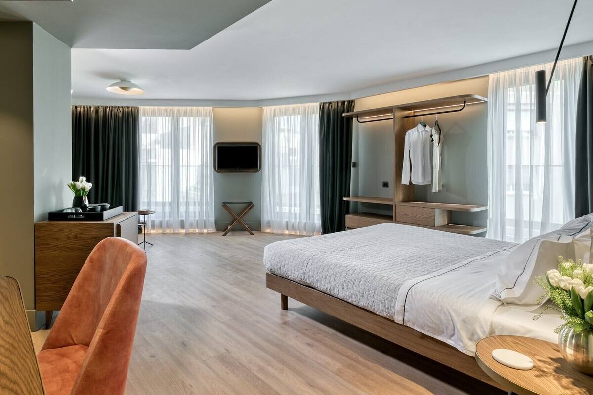 Moderni hotellihuone, jossa on suuri sänky, työpöytä tuolilla, vaatekaappi ja seinälle asennettu televisio.