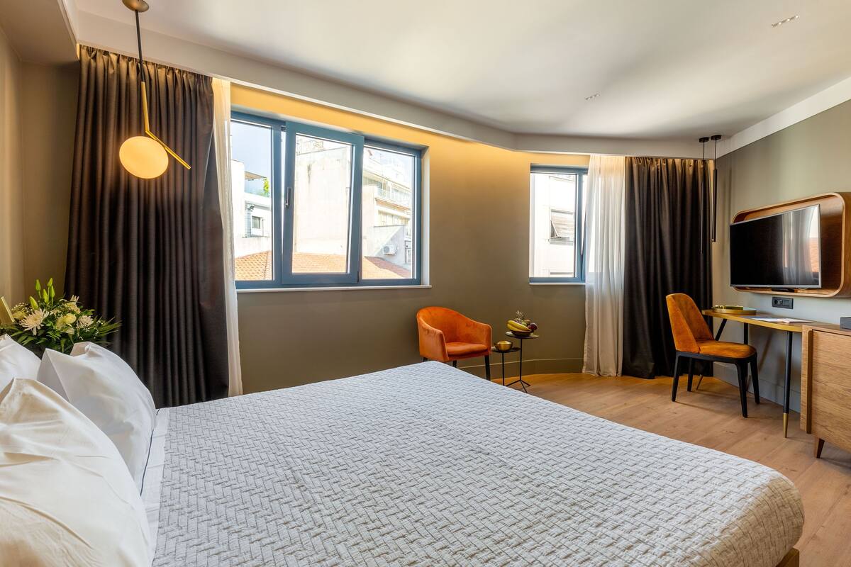 Hotellihuone, jossa on suuri sänky, työpöytä, kaksi tuolia, televisio ja ikkuna, jossa on verhot.