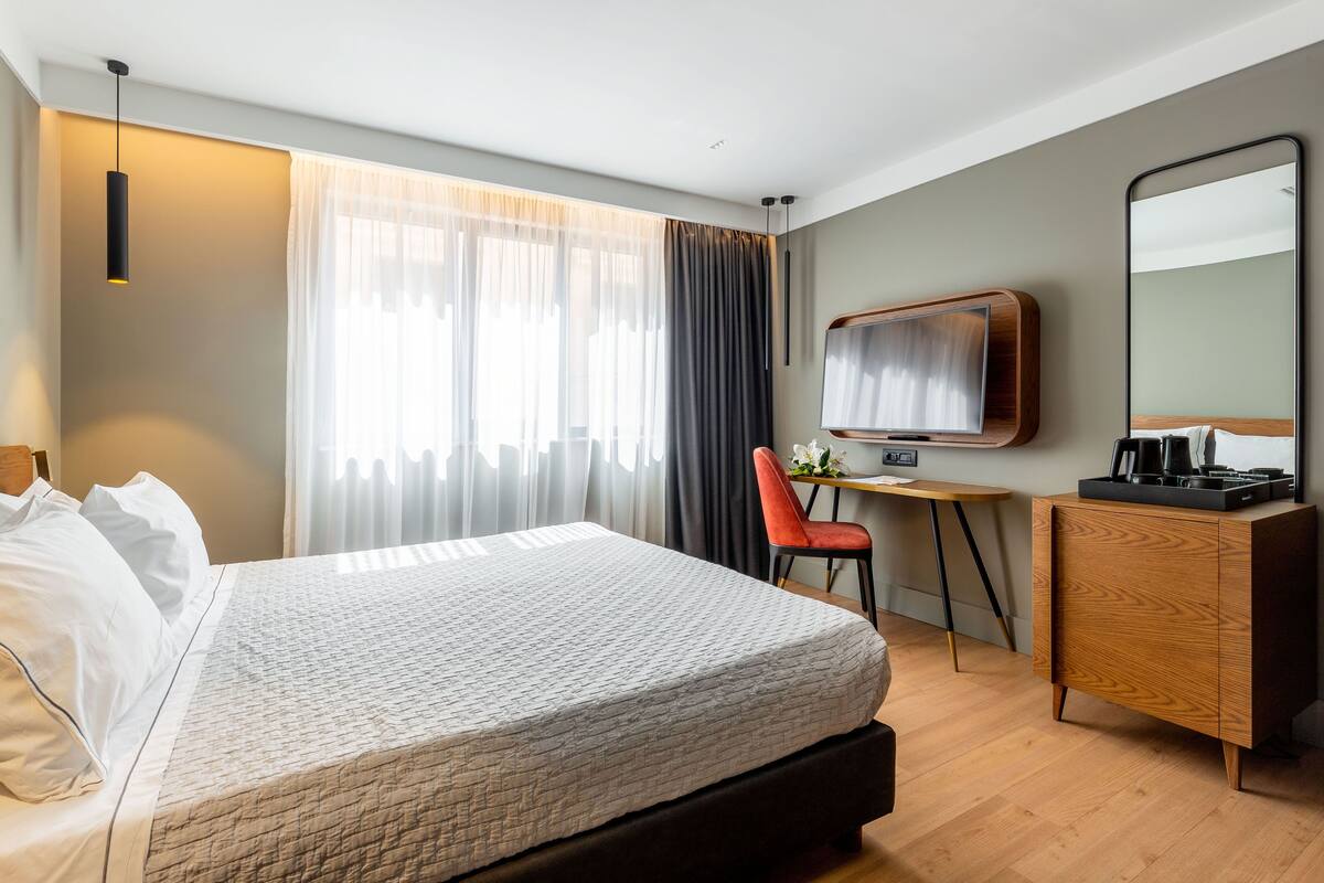 Moderni hotellihuone, jossa on suuri sänky, työpöytä, tuoli, televisio ja vaatekaappi.