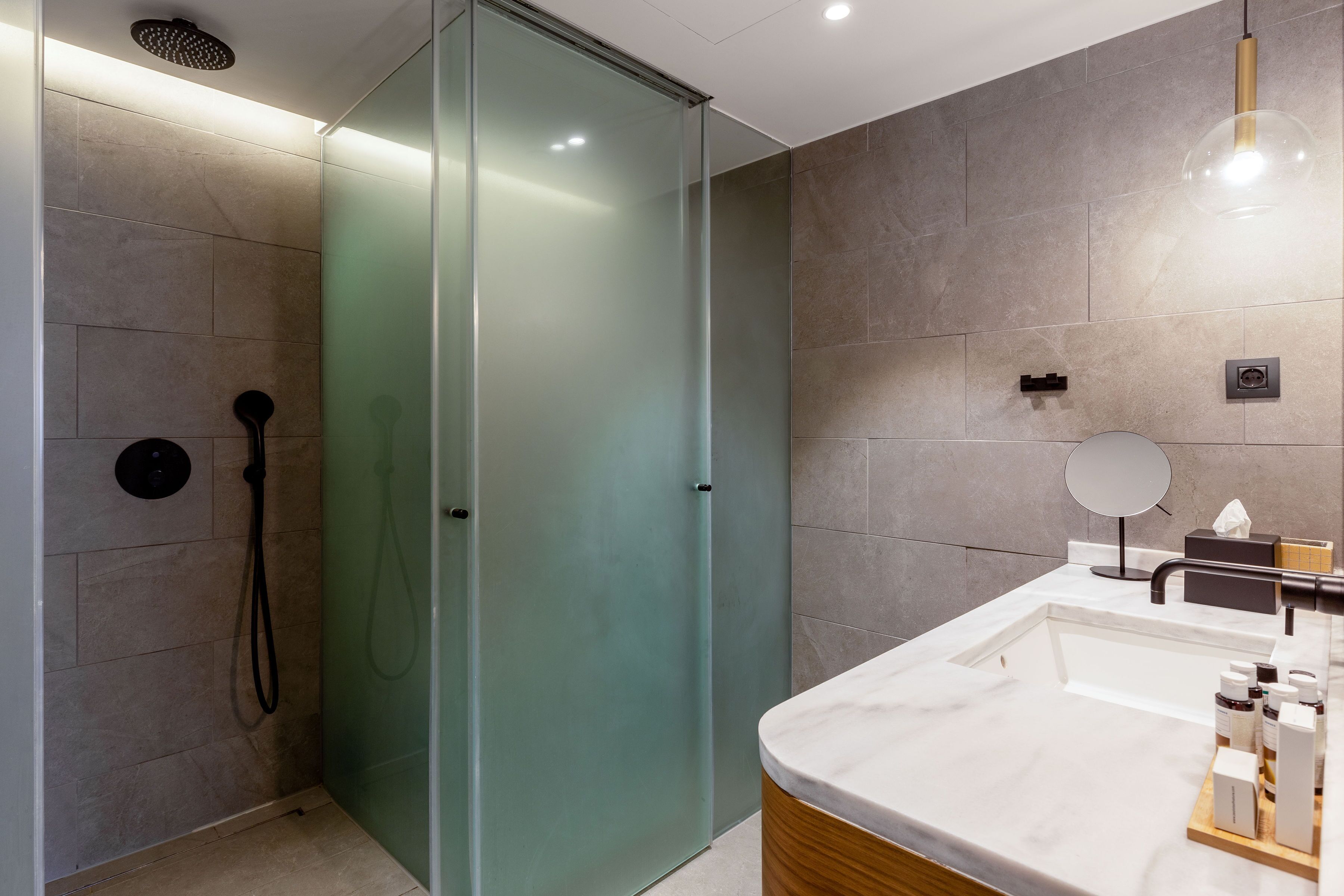 A modern bathroom with a glass shower enclosure, a marble sink, and a wooden vanity.