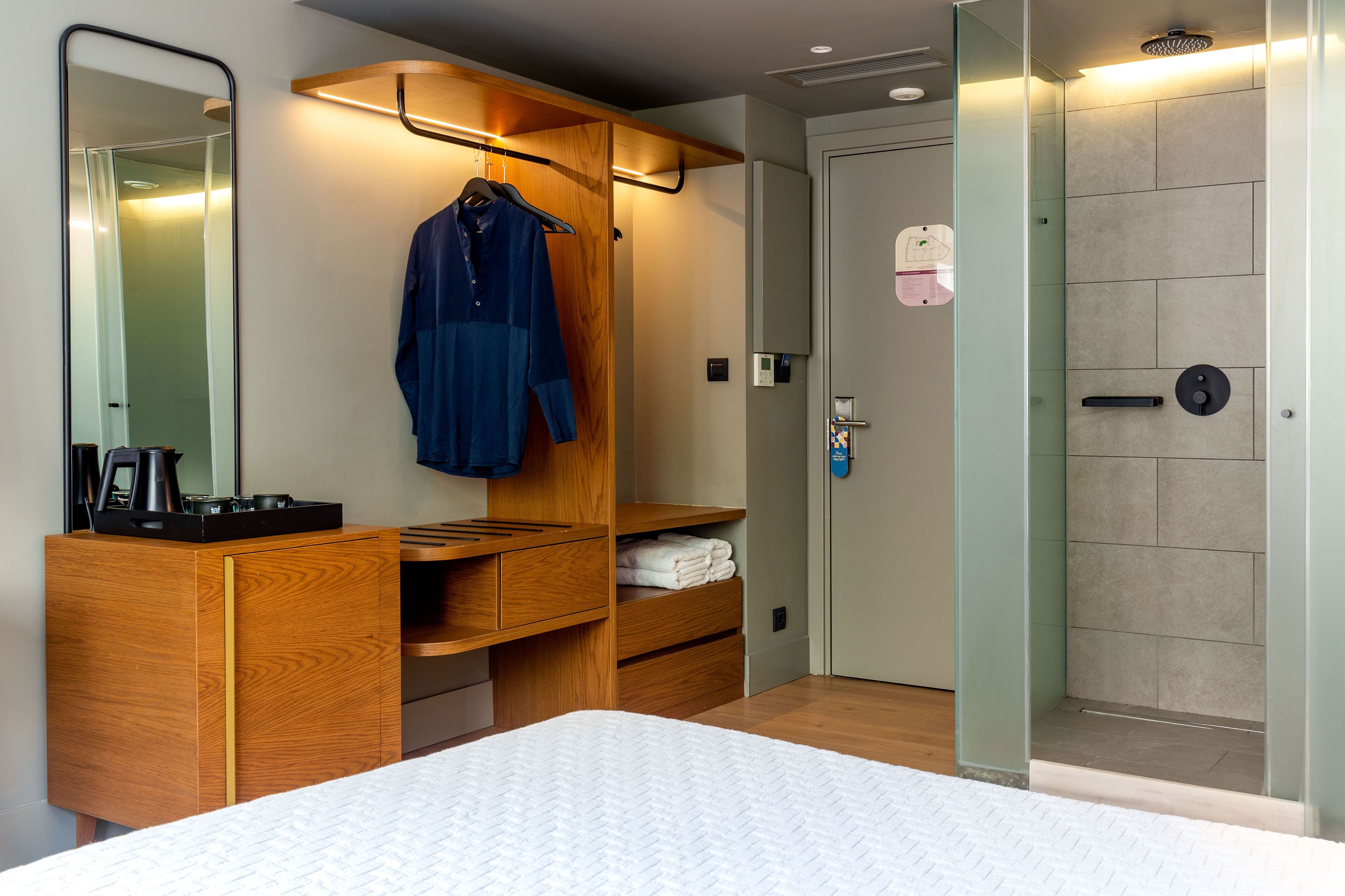 A hotel room with a bed, wooden wardrobe, and a shower area.