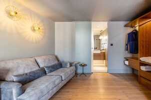 Uma sala de estar moderna com um sofá cinzento, piso de madeira e um guarda-roupa de madeira com roupas e toalhas.
