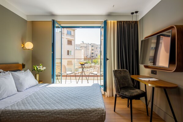Une chambre d’hôtel équipée d’un lit, d’un bureau, d’une chaise, d’une télévision et d’un balcon offrant une vue sur les bâtiments.