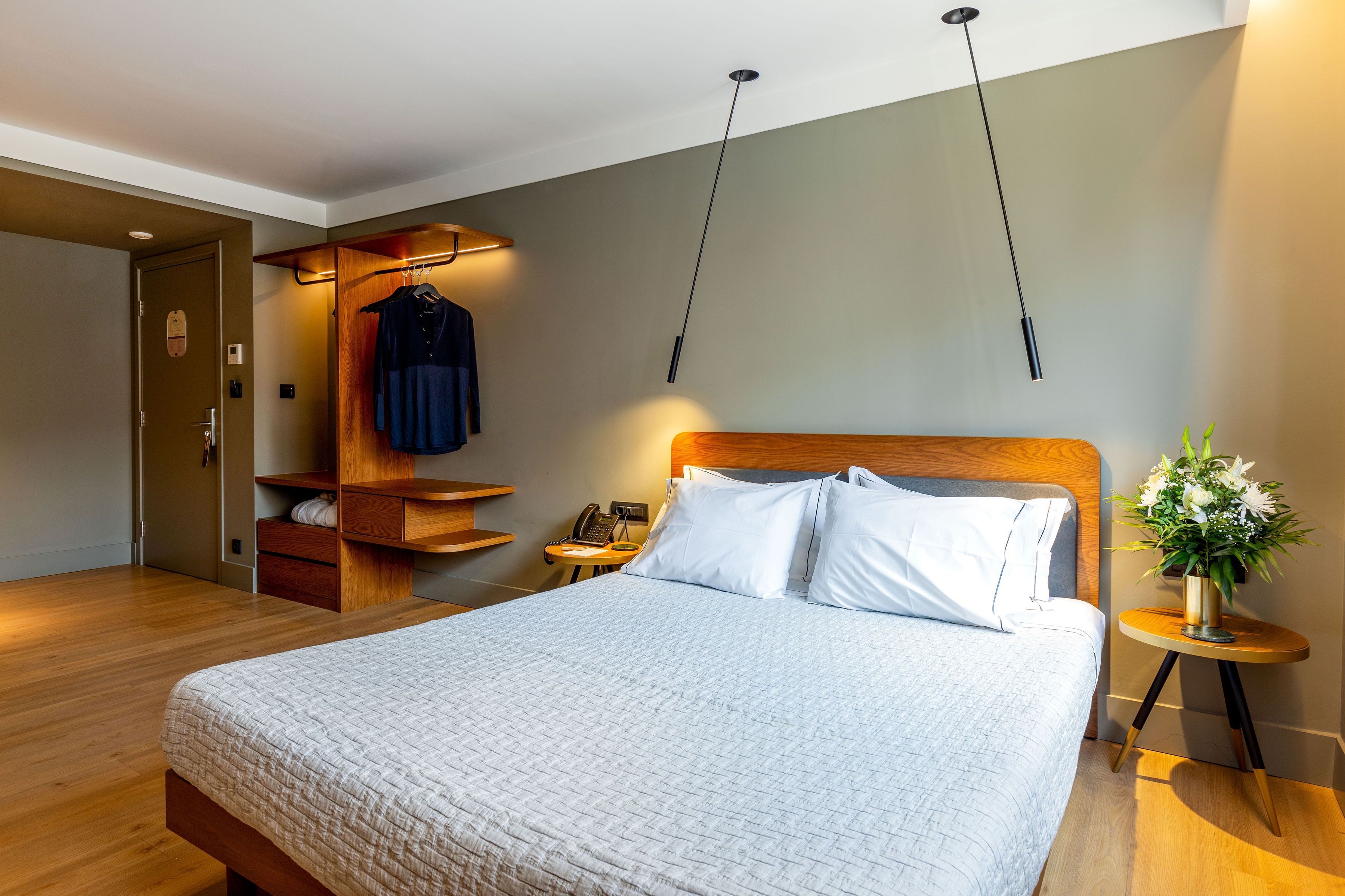 Een netjes ingerichte hotelkamer met een groot bed, een houten hoofdbord, een nachtkastje met een lamp, een klein bureau met een telefoon en een kapstok.