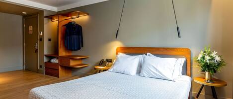 Een netjes ingerichte hotelkamer met een groot bed, een houten hoofdbord, een nachtkastje met een lamp, een klein bureau met een telefoon en een kapstok.
