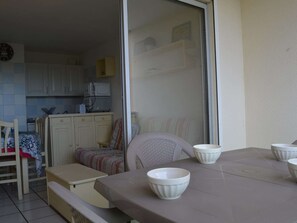 A dining area with a table, chairs, and white bowls. There is a kitchen in the background with cabinets and appliances. - 2-room apartment by the sea with pool, parking, Saint-Cyprien Beach (Saint-Cyprien)