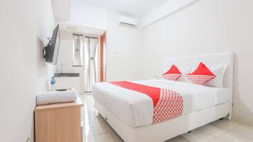 A hotel room with a bed, a bedside table, a TV mounted on the wall, and a window with curtains.