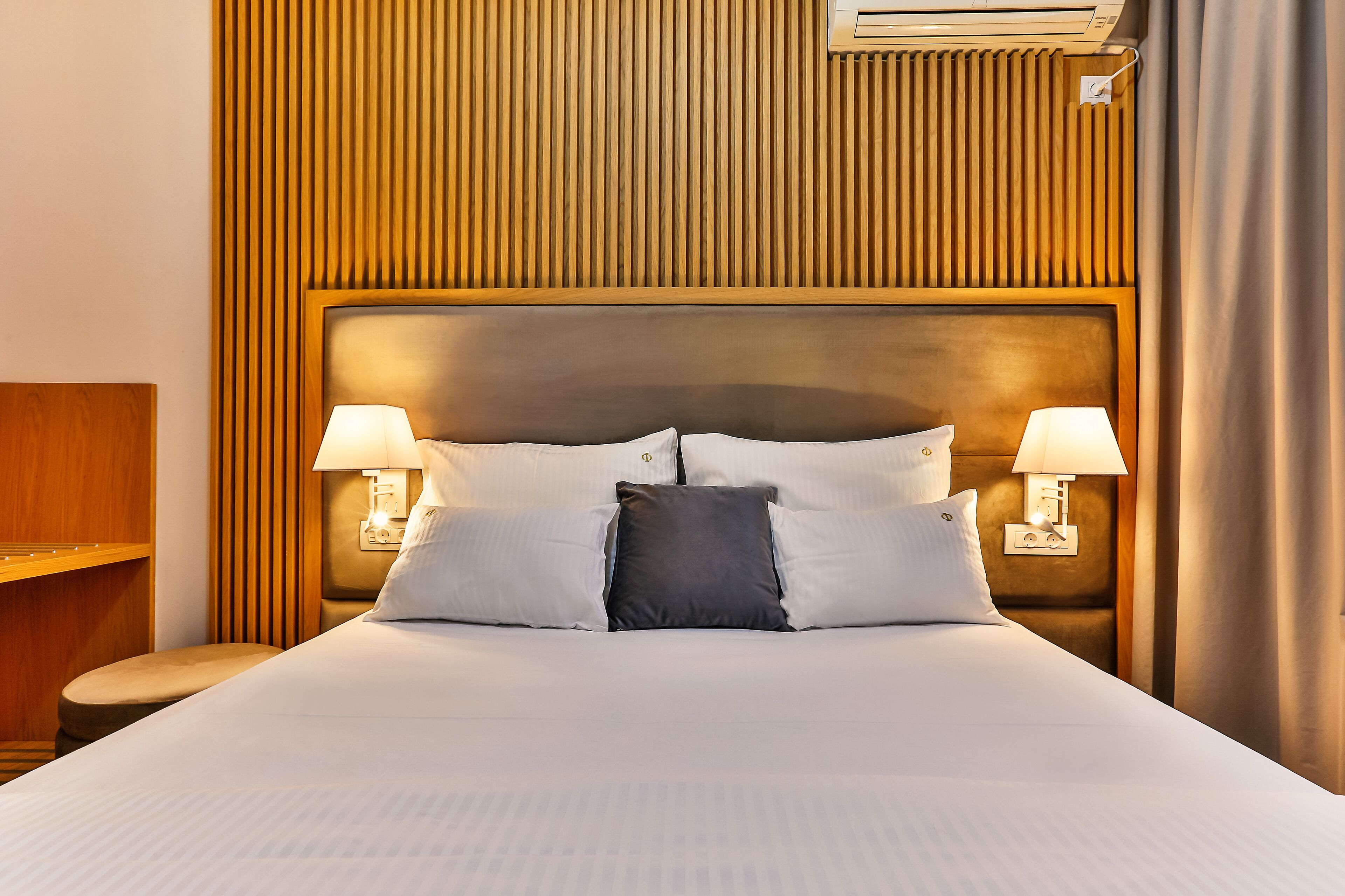 A neatly made bed with a headboard, two bedside lamps, and a wooden panel wall.