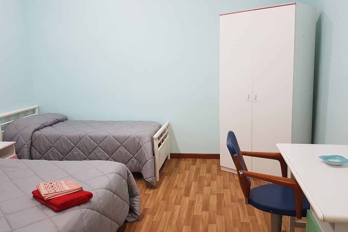 A dormitory room with two beds, a wardrobe, a desk, and a chair.