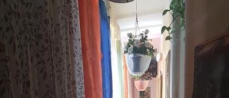 Un pasillo con cortinas estampadas, una maceta colgante y un suelo de baldosas.