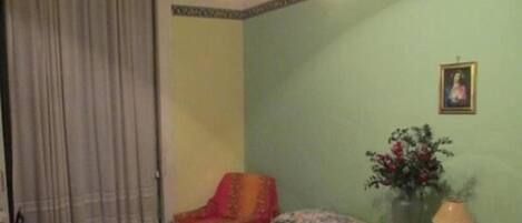 A room with a bed, a chair, a vase with flowers, and a lamp on a side table.