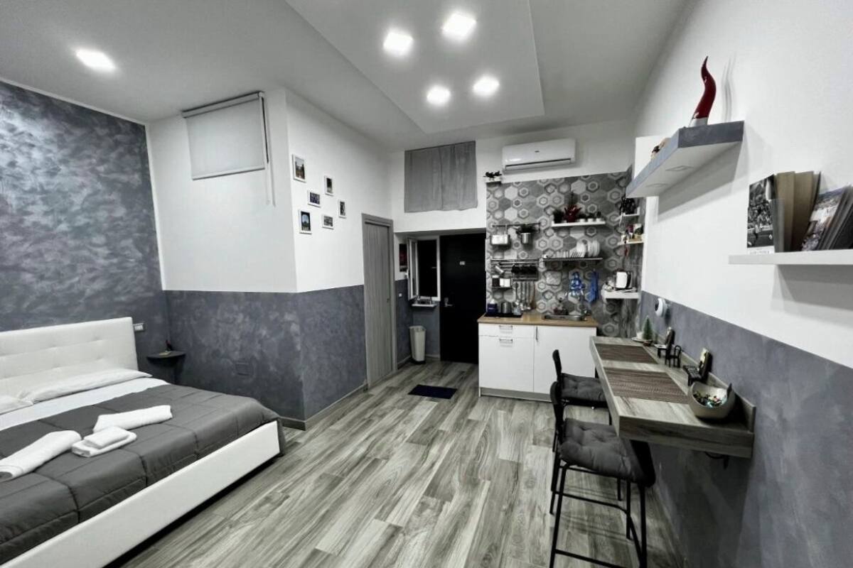 A modern bedroom with a bed, a desk, and a kitchenette.