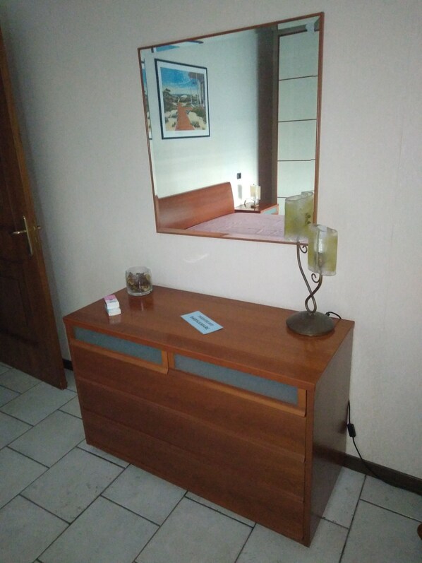 A wooden dresser with a mirror above it, a small card, and a glass on the dresser. - B&B by the sea, large double room with private bathroom and balcony overlooking the sea. (Salerno)