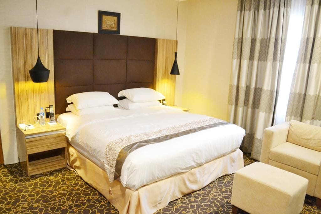 A hotel room with a large bed, bedside tables, a chair, and a patterned carpet.