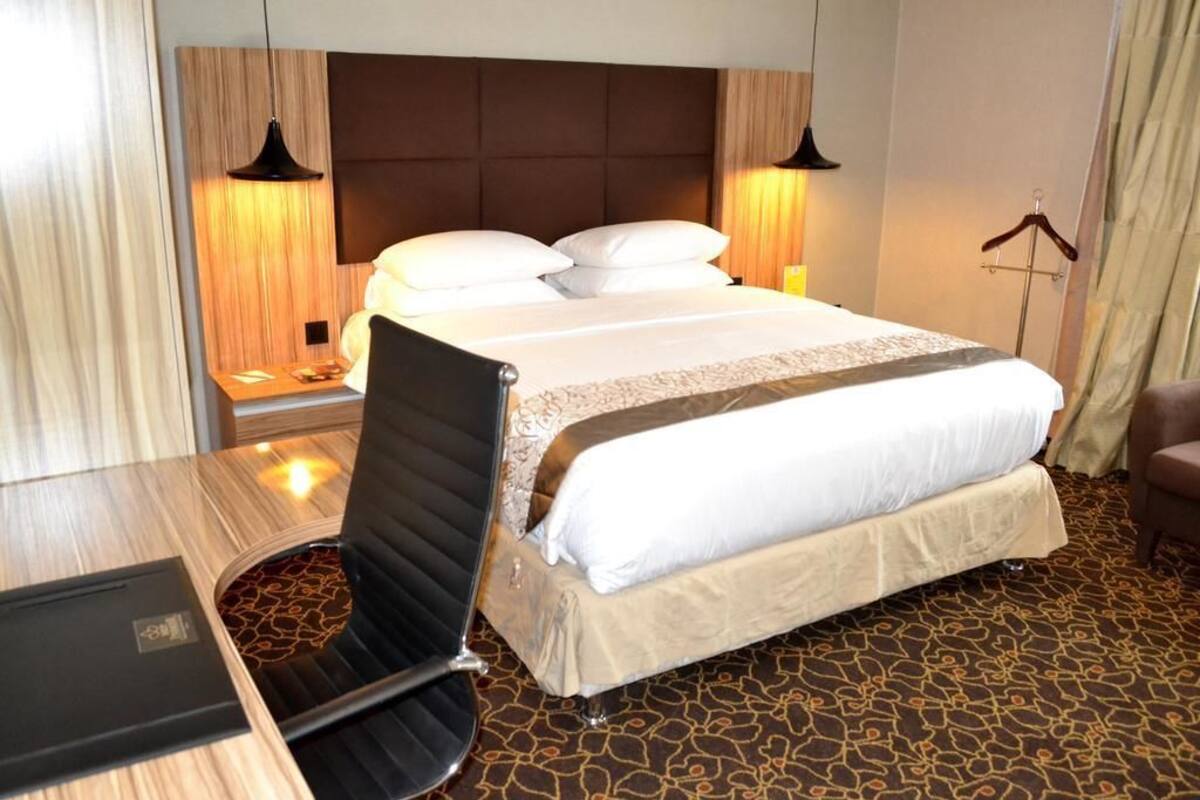 A hotel room with a large bed, a desk, and a chair. There are two lamps on either side of the bed.